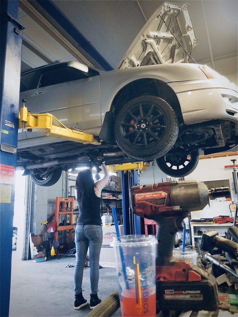 Kaila working under a silver Subaru on a lift