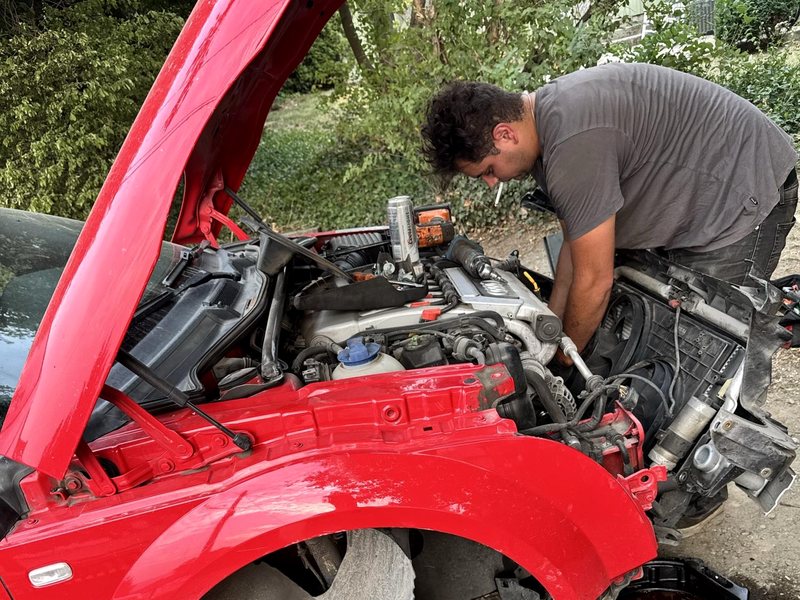 Mechanic working in the engine bay of a red car with the front end removed during a roadside radiator replacement
