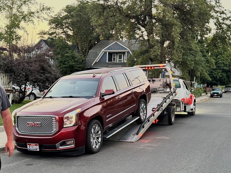 Maroon GMC Yukon Denali XL on a residential street next to a flatbed